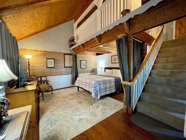 Ein gemütliches Schlafzimmer mit einem Bett, einem Schreibtisch mit Lampe, einem Sessel und einer Treppe.