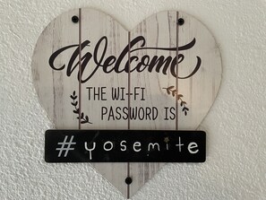 Señal en forma de corazón con el texto 'Bienvenido' y 'La contraseña de Wi-Fi es #yosemite' en una pared con textura.