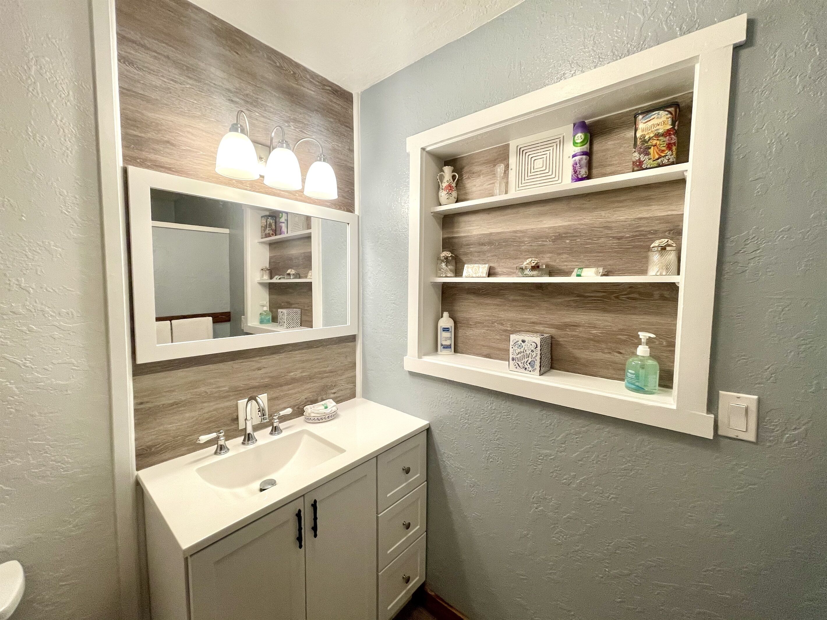 Een badkamer met een witte wastafel, een spiegel en een plank met toiletartikelen.