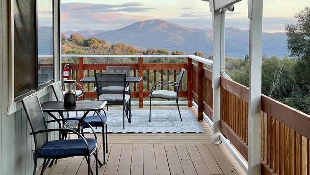 Eine Holzterrasse mit Tisch und Stühlen, mit Blick auf eine gebirgige Landschaft.