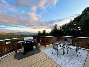 Una terraza con una parrilla, mobiliario exterior y una vista panorámica de montañas y árboles.