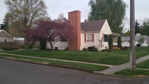 A single-story house with a brick chimney, a small porch, and a well-maintained lawn.
