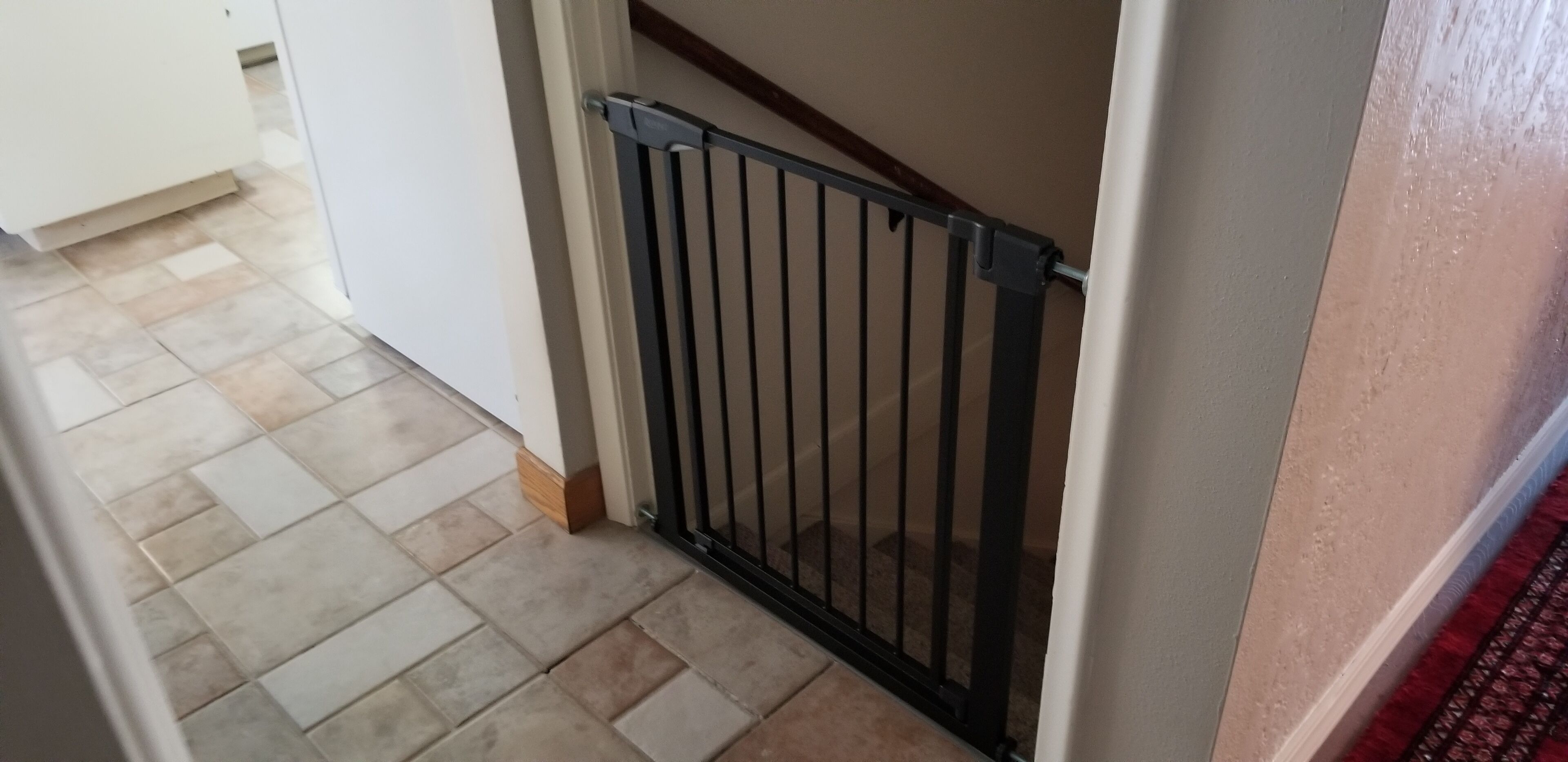 Ein Korridor mit gefliestem Boden, einem schwarzen Metallgitter und einer weißen Wand.