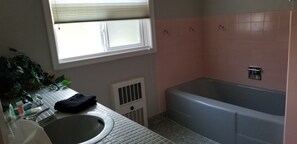 A bathroom with a bathtub, a sink, a window, and a radiator. - Charming Home In Quiet, Friendly Grangeville, Idaho Sleeps 9 Guests (Grangeville)