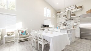 A spacious kitchen with white cabinetry, a stainless steel refrigerator, and a dining area with a white table and chairs. - Adorable 4 Bedroom Guest House wPool + Jacuzzi (Poway)