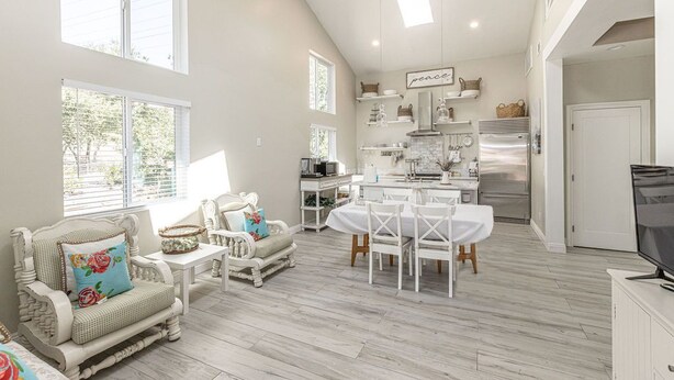 A spacious living area with a dining table and chairs, a kitchen with modern appliances, and large windows providing natural light. - Adorable 4 Bedroom Guest House wPool + Jacuzzi (Poway)