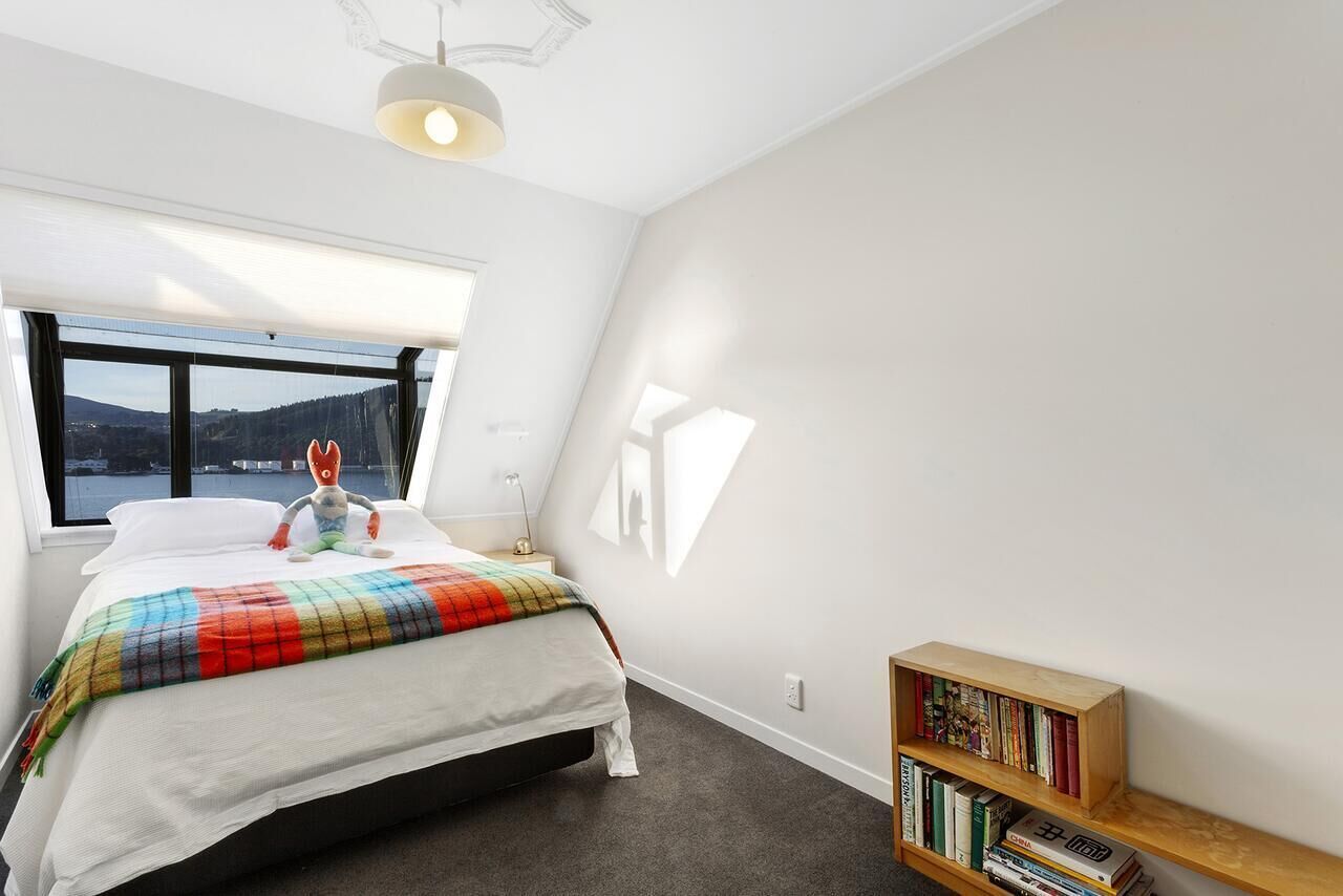 A bedroom with a bed, a window with a view, a bookshelf, and a ceiling light.