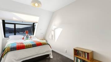 A bedroom with a bed, a window with a view, a bookshelf, and a ceiling light.