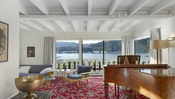 A spacious room with a grand piano, a large window offering a scenic view of a lake and mountains, and a red patterned carpet.