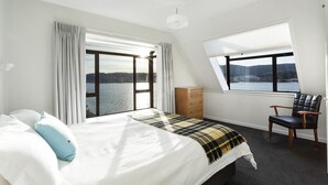 Una camera da letto con un letto grande, una cassettiera, una sedia e una finestra con vista sull'acqua.