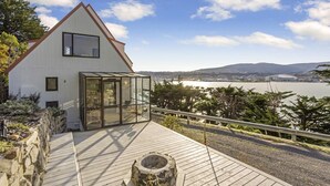 Una casa moderna con veranda in vetro, terrazza in legno e vista su un lago e montagne.