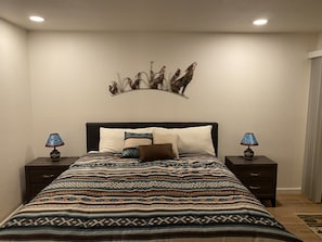 Un dormitorio con una cama grande, dos mesitas de noche, un cuadro en la pared y una colcha estampada.