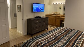 Ett sovrum med en säng, en byrå, en tv och ett badrum med handfat och spegel.