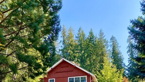 A red barn-style house with a covered porch and a small deck, surrounded by trees and a well-maintained lawn.
