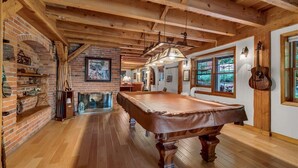 A spacious room with a pool table, wooden beams, brick walls, and a fireplace.
