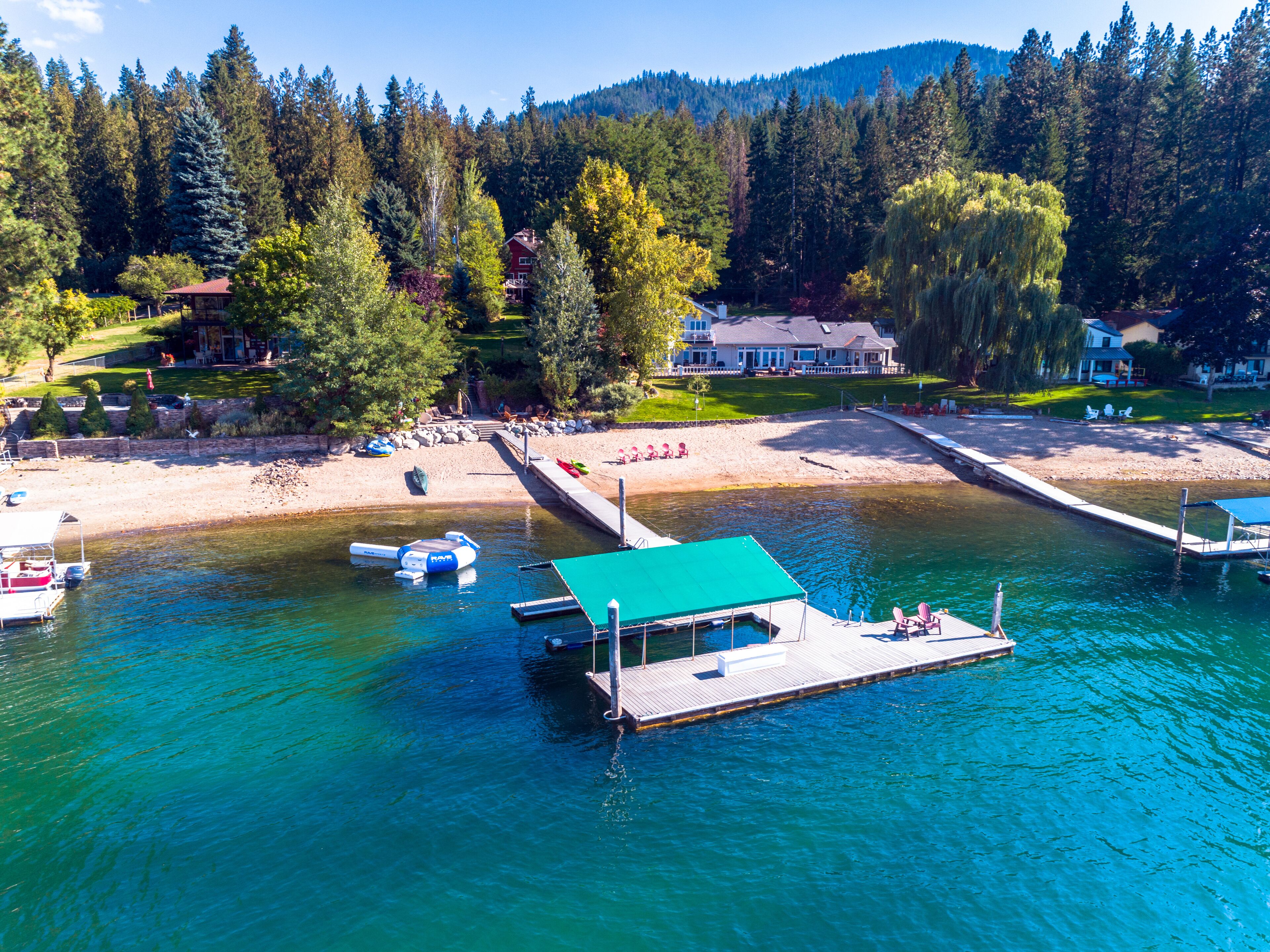 A lakeside property with a dock, boats, and a house surrounded by trees.