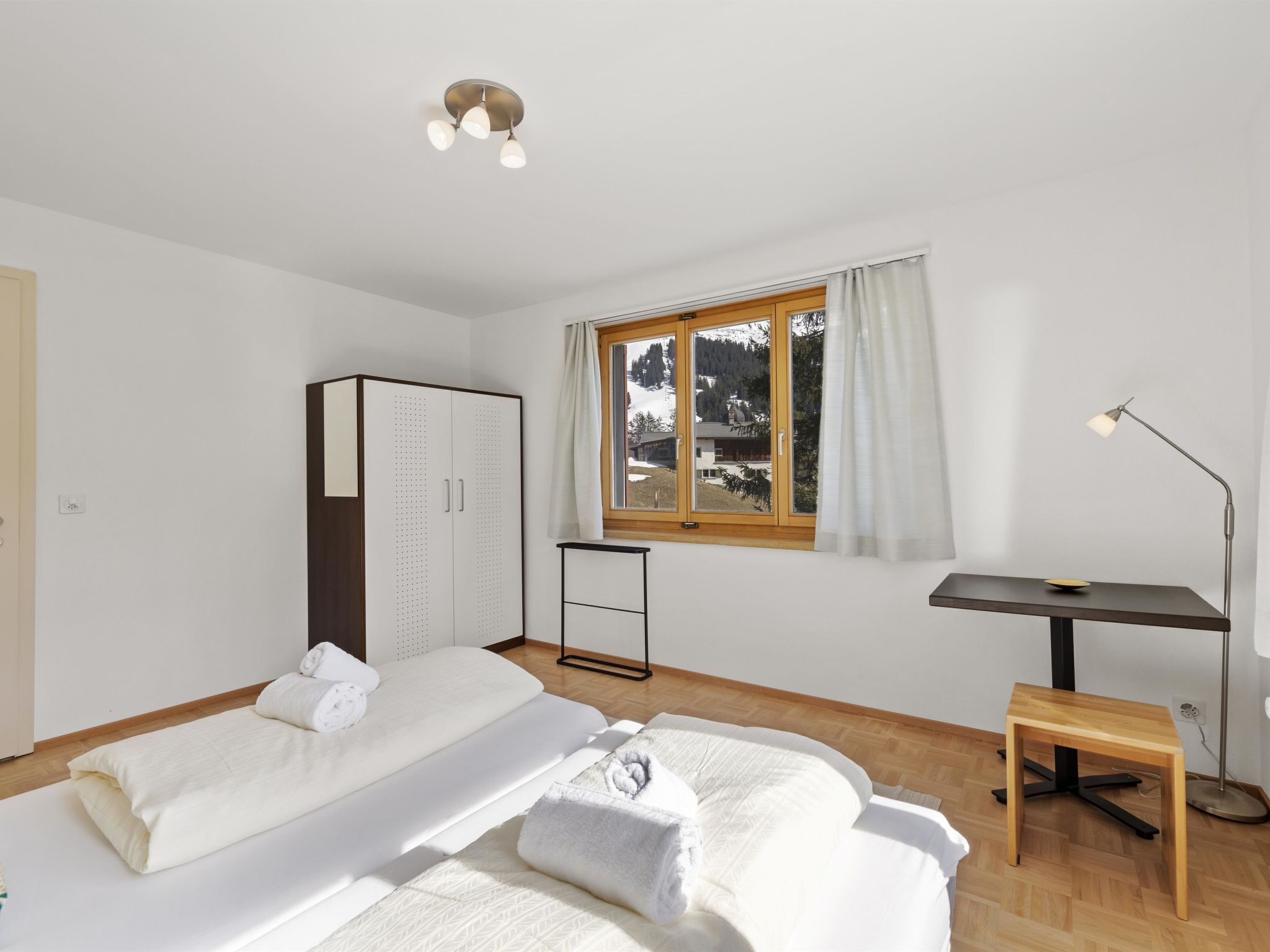 Une chambre avec deux lits, une armoire, un bureau et une fenêtre donnant sur un paysage enneigé.