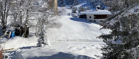 A snow-covered village with a church tower, a wooden building, and a ski slope in the background.