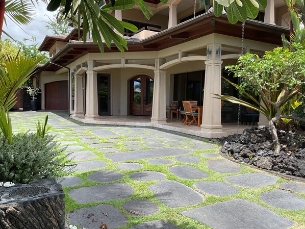 Una casa con un patio empedrado de piedra, sillas de madera y un gran árbol.