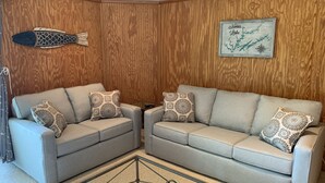 A corner living room with two grey sofas, patterned cushions, a wooden paneled wall, a fish decoration, and a framed map of Norris Lake. - Luxury Norris Lake Getaway - Perfect for Families & Groups - Lake Front w Dock! (Caryville)