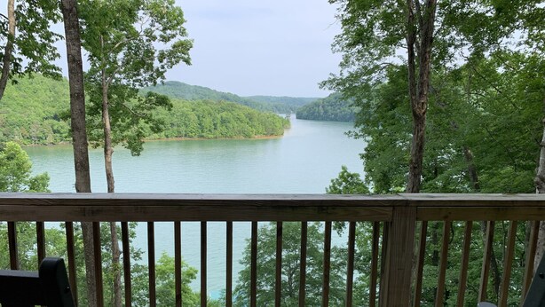 A wooden deck with two chairs and a table, overlooking a lake surrounded by trees. - Luxury Norris Lake Getaway - Perfect for Families & Groups - Lake Front w Dock! (Caryville)