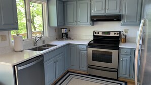 A modern kitchen with grey cabinets, stainless steel appliances, a built-in oven, and a window providing natural light. - Luxury Norris Lake Getaway - Perfect for Families & Groups - Lake Front w Dock! (Caryville)