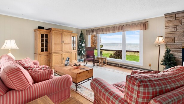A living room with a large window, a wooden cabinet, a sofa, and a small table. - Amazing waterfront and sunset views! (Indian River)