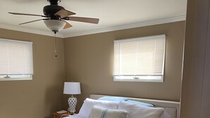 A bedroom with a bed, a ceiling fan, two windows with blinds, a bedside lamp, and a carpeted floor. - Amazing waterfront and sunset views! (Indian River)