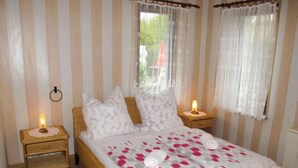 Un dormitorio con una cama, dos mesitas de noche, una ventana con cortinas y vistas a zonas verdes.