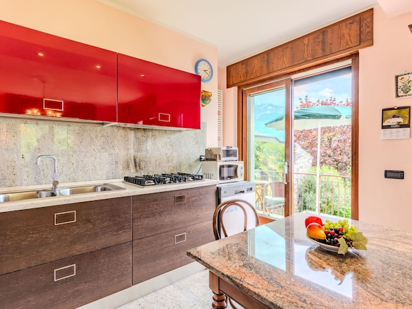 A modern kitchen with red cabinets, a granite countertop, and a view of a balcony with a patio umbrella.