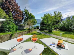 A garden patio with two tables, each with a glass of red wine, and a magazine on one table.