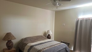 Ein Schlafzimmer mit einem Bett, zwei Nachttischlampen, einem Deckenventilator und einem Fenster mit Vorhängen.