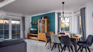 Un comedor con una mesa y sillas de madera, un televisor sobre un mueble bajo y un armario con puertas de cristal.