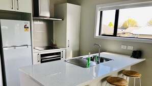 Une cuisine moderne dotée d’un réfrigérateur en acier inoxydable, d’un four encastré, d’un évier avec un robinet et d’une fenêtre située au-dessus de l’évier. On trouve trois tabourets en bois près de l’îlot de la cuisine.