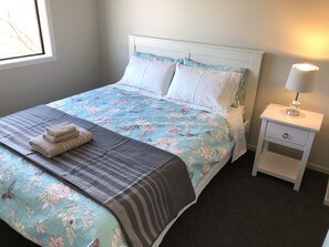 A neatly made bed with a floral bedspread, a striped blanket, and folded towels. There is a bedside table with a lamp and a drawer. - Central Stadium Apartments (Hamilton)