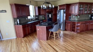 A spacious kitchen with wooden cabinets, a central island, and a stainless steel refrigerator. - Massive Spacious House with Views, Adventure and Location (Colorado Springs)