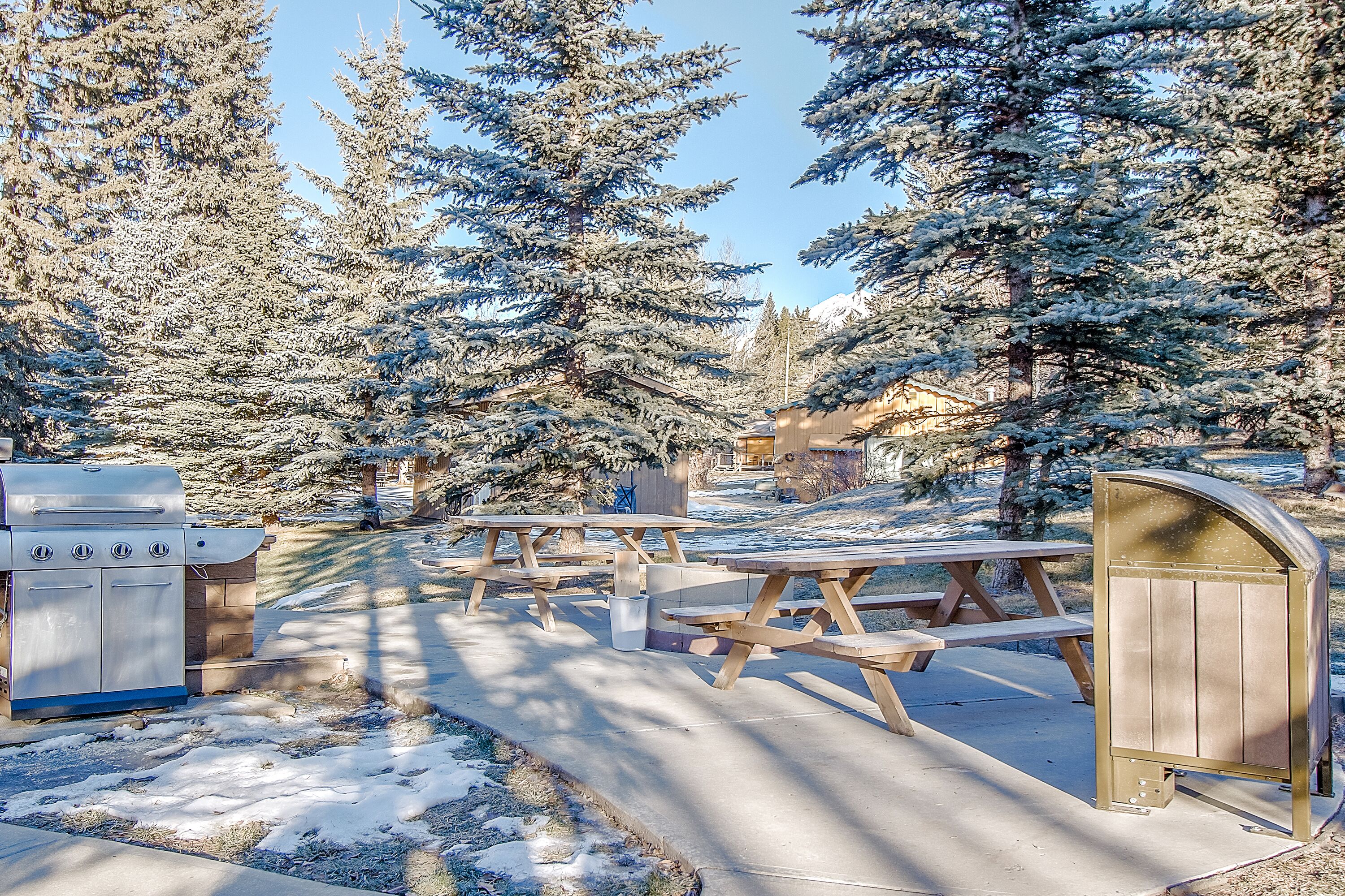 A snow-covered picnic area with wooden benches and a barbecue grill.