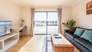 Una sala de estar moderna con televisor de pantalla plana, un sofá, una mesa de centro y vista a un área pavimentada exterior.