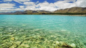 Un lago transparente con rocas visibles y montañas al fondo.