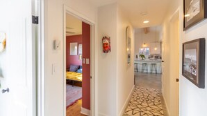 A hallway leading to a bedroom with a bed, a kitchen area with stools, and a patterned floor.