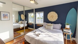 A bedroom with a bed, a ceiling fan, a large mirror, and a surfboard decoration.