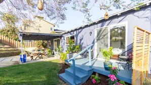 A house with a covered patio, a staircase leading to a deck, and a small garden area with flowers and plants.