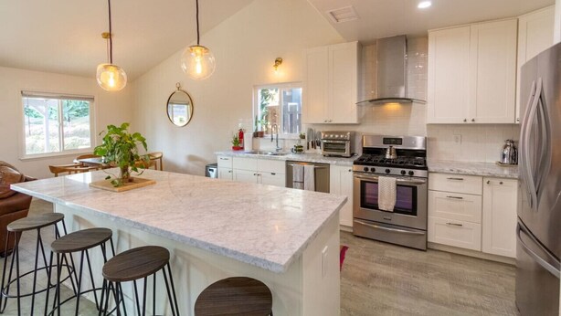 A modern kitchen with white cabinets, a large island with stools, stainless steel appliances, and pendant lighting.