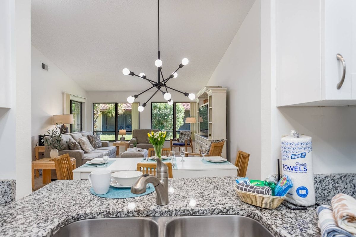 A modern kitchen with granite countertops, a stainless steel sink, and a dining area with a white table and chairs.