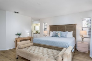 A bedroom with a large bed, bedside tables, a bench, and a mirror. - Villa on Quiet Cul-De-Sac | Heated Pool and Spa (Sarasota)