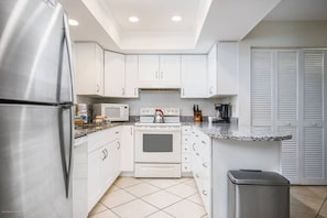 A modern kitchen with white cabinets, a stainless steel refrigerator, a microwave, an oven, and a granite countertop. - Villa on Quiet Cul-De-Sac | Heated Pool and Spa (Sarasota)