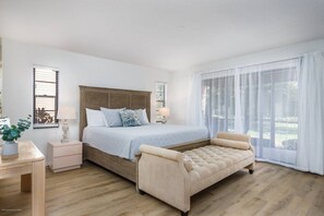 A bedroom with a bed, bedside tables, a bench, and large windows. - Villa on Quiet Cul-De-Sac | Heated Pool and Spa (Sarasota)