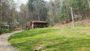 A cabin with a porch and a dirt path leading to it, surrounded by trees.
