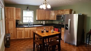 A kitchen with wooden cabinets, a stainless steel refrigerator, a wooden dining table with four chairs, and a window providing natural light.
