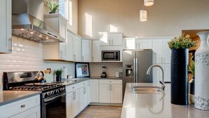 A modern kitchen with white cabinetry, stainless steel appliances, and a central island with a sink. - Sleeps 12~Great View! UNR~Deck~Reno~Minerva House~ Near Downtown~Family Fun (Reno)